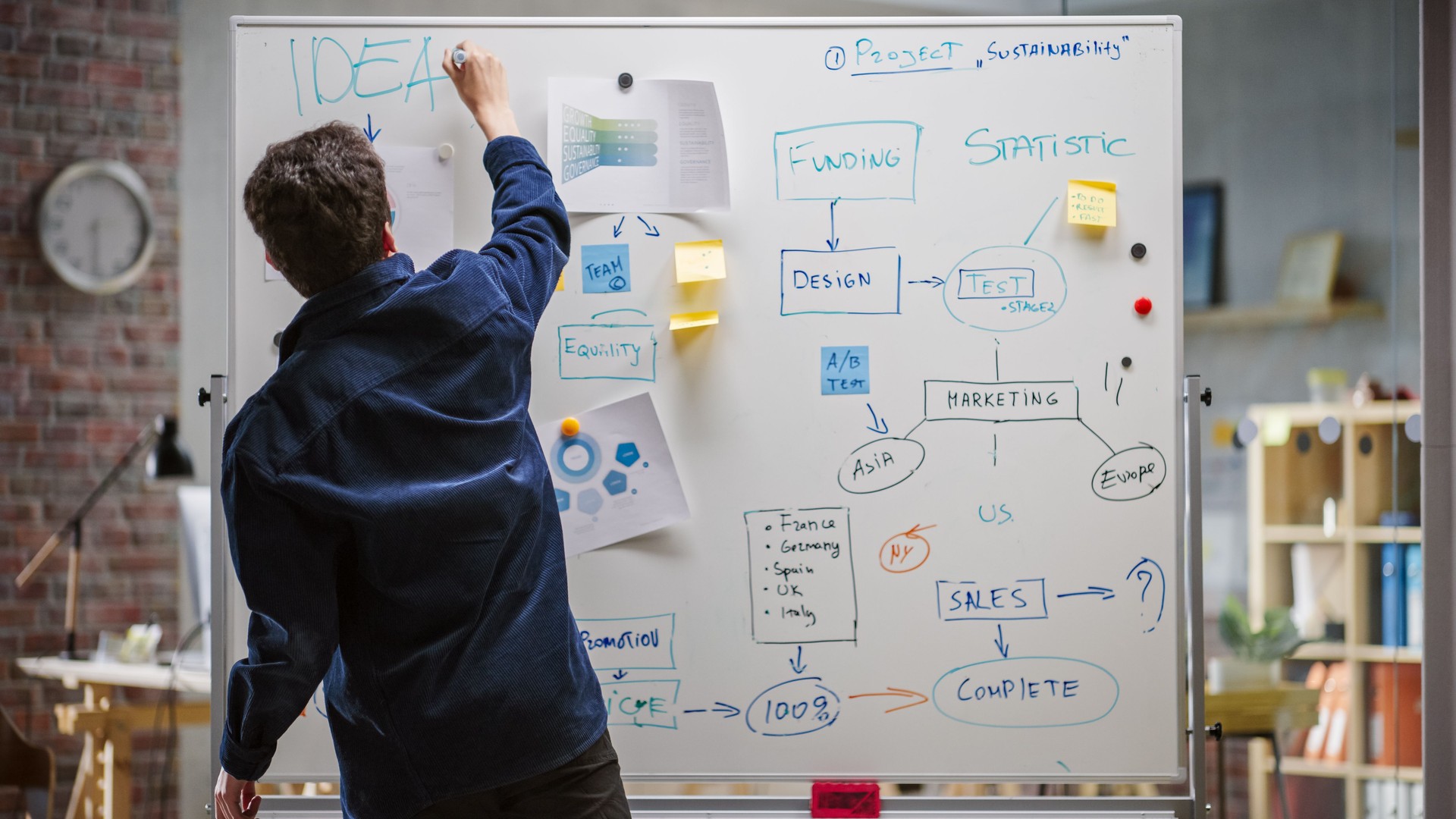 Young Project Manager Using Charts and Statistics and Writing on a Whiteboard. Digital Content Specialist Brainstorming For a Marketing Campaign in an Office. Back View Shot.